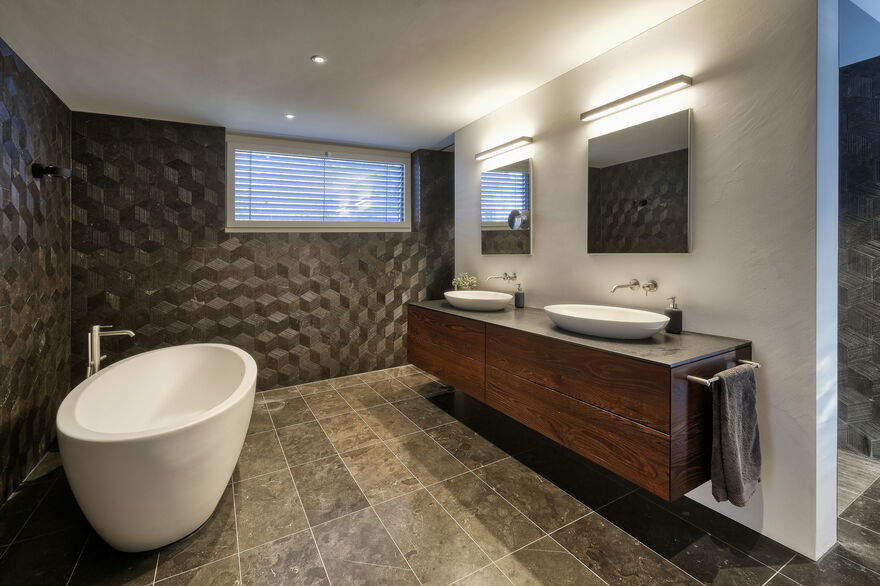 Badezimmer mit freistehender Badewanne, dunklen Wänden und Bodenplatten und einem Lavaboschrank aus Holz, Badezimmer-Umbau realisiert durch DIE SCHREINER